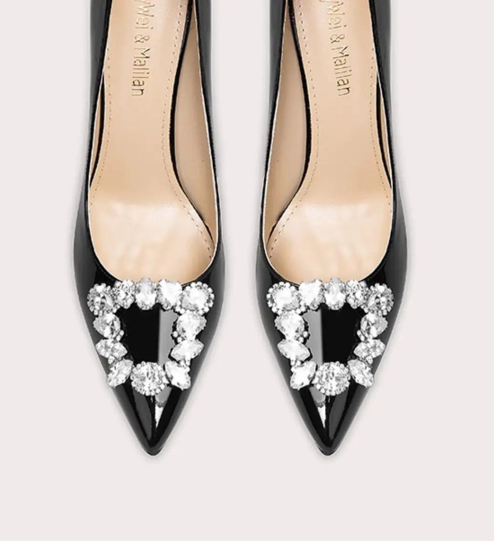 Black high-heeled shoes with decorative heart-shaped embellishments on a light gray background