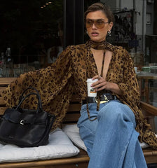 Woman in leopard print top and blue jeans sitting on a bench with a black handbag and coffee cup.