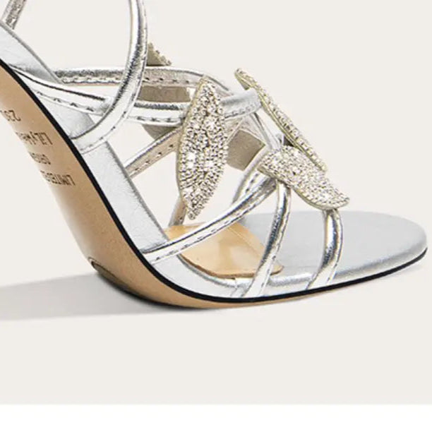 Silver high-heeled shoe with decorative strap on a white background