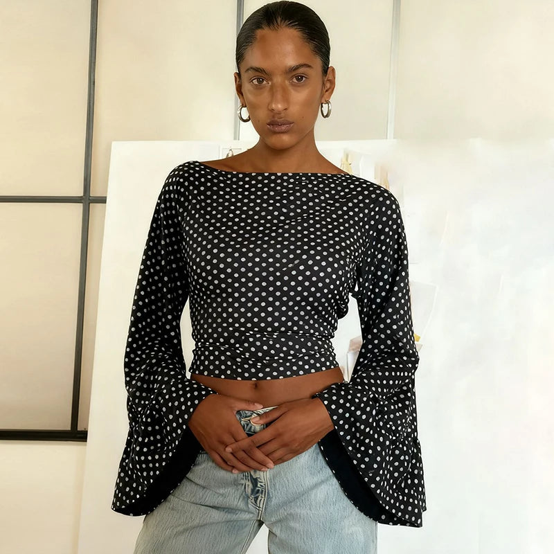 Woman wearing a black and white polka dot top with bell sleeves against a neutral background
