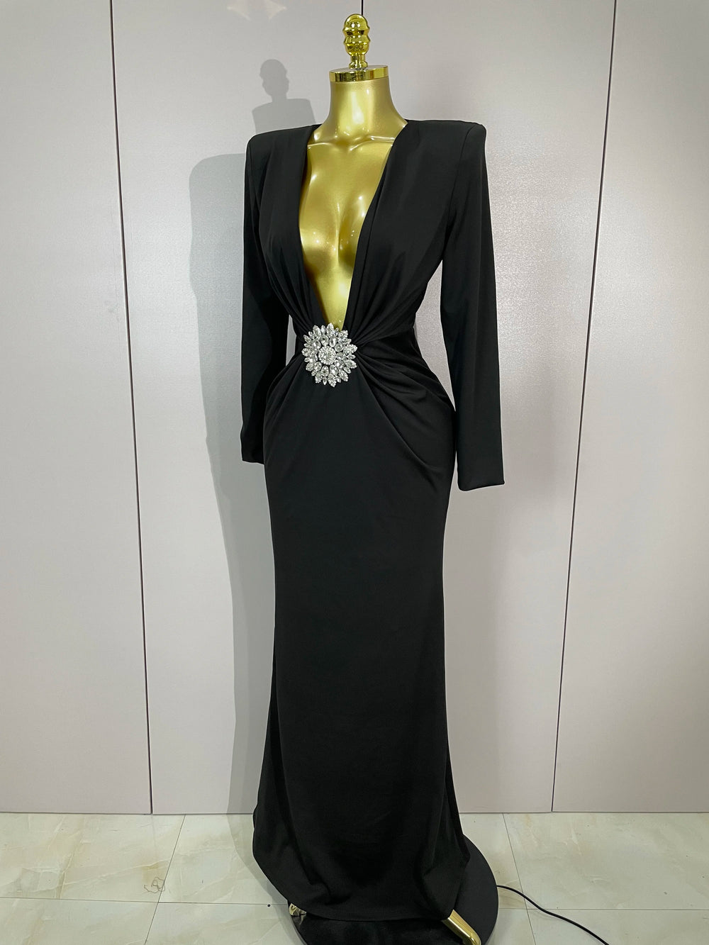 Black evening gown with a large brooch on a mannequin against a plain background
