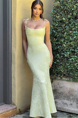 Woman in a light green evening gown standing against a wall with greenery.