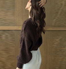 Woman wearing a dark brown sweater and light-colored pants against a wooden panel background