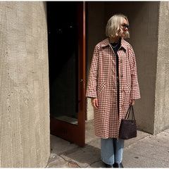 Person wearing a red and white checkered coat standing against a textured wall.