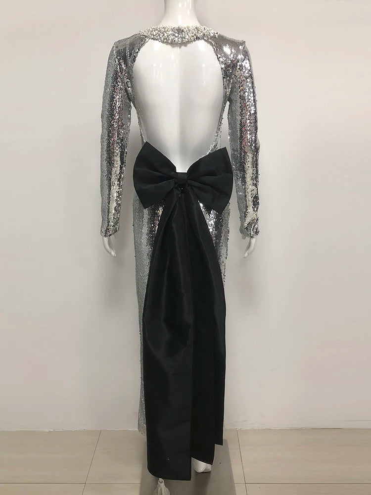 Mannequin wearing a silver sequin dress with long sleeves and a black bow at the back on a white background.