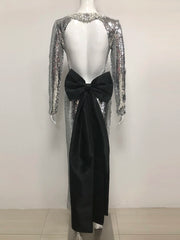 Mannequin wearing a silver sequin dress with long sleeves and a black bow at the back on a white background.