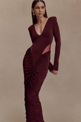 Woman wearing a burgundy evening gown with long sleeves and ruched details on a beige background