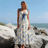 Blue floral print one-piece swimsuit and flowing skirt worn by a model on a rocky beach.