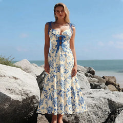 Blue floral print one-piece swimsuit and flowing skirt worn by a model on a rocky beach.