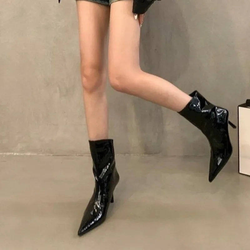 Black patent leather ankle boots worn by a person on a neutral background