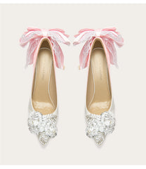 Pair of high-heeled shoes with decorative bows and embellishments on a light background