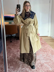 Woman in a trench coat with navy sailor collar and leopard print skirt, taking a mirror selfie