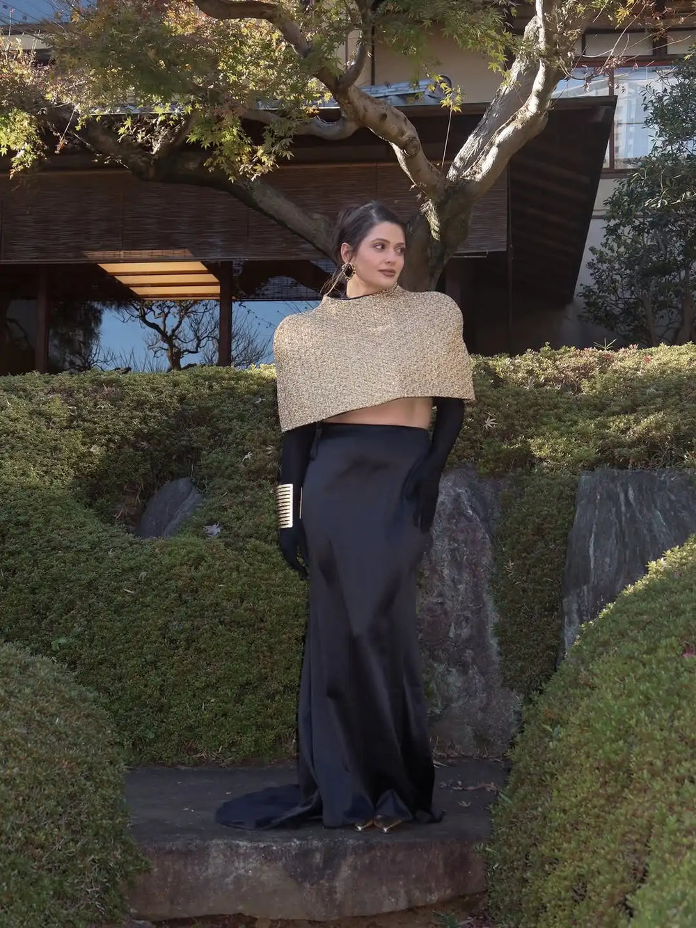 Woman in a beige top and black pants standing in a garden setting