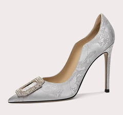 Silver high-heeled shoe with floral lace design and decorative buckle on a light gray background