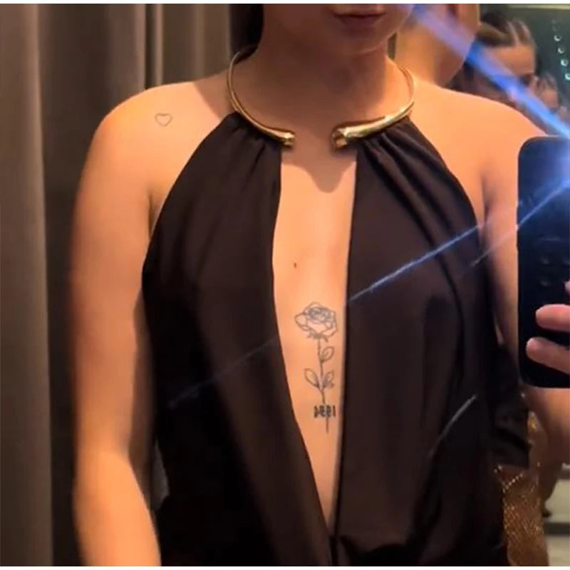 Person wearing a black halter top with a gold collar, holding a phone.