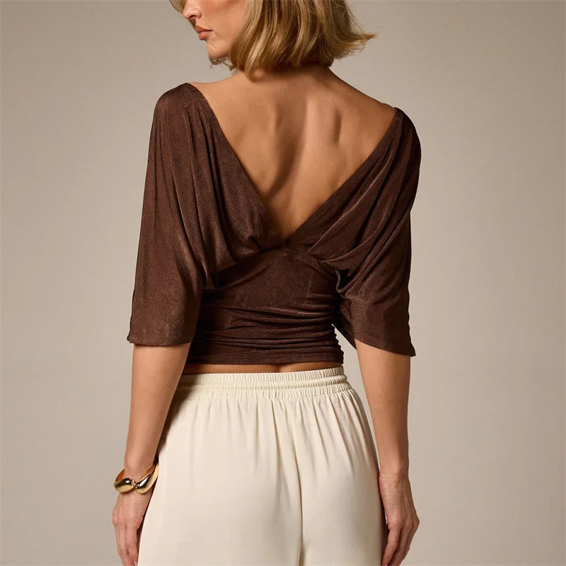 Woman wearing a brown open-back top and beige pants on a neutral background
