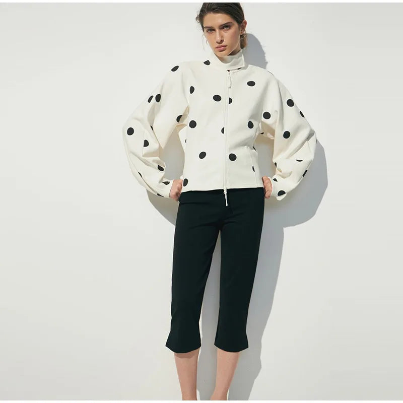 Woman wearing a white jacket with black polka dots and black pants on a white background