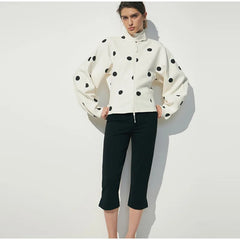 Woman wearing a white jacket with black polka dots and black pants on a white background