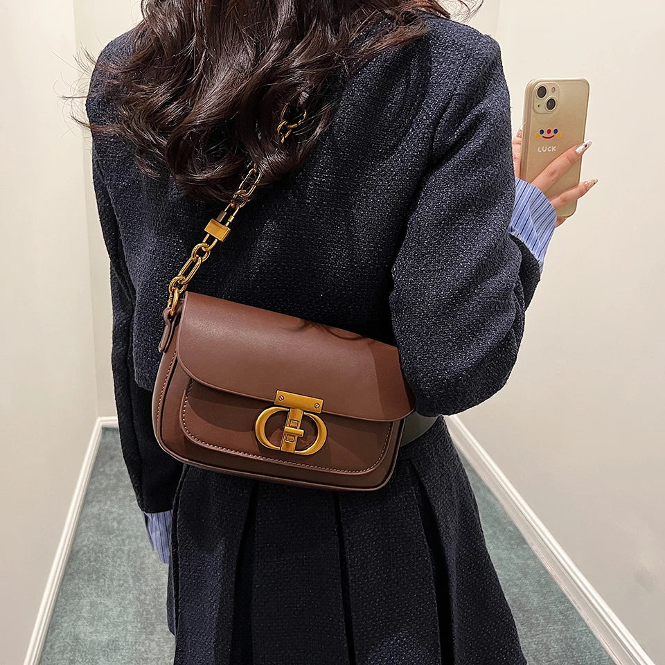 Person wearing a brown leather bag with gold hardware, taking a mirror selfie.