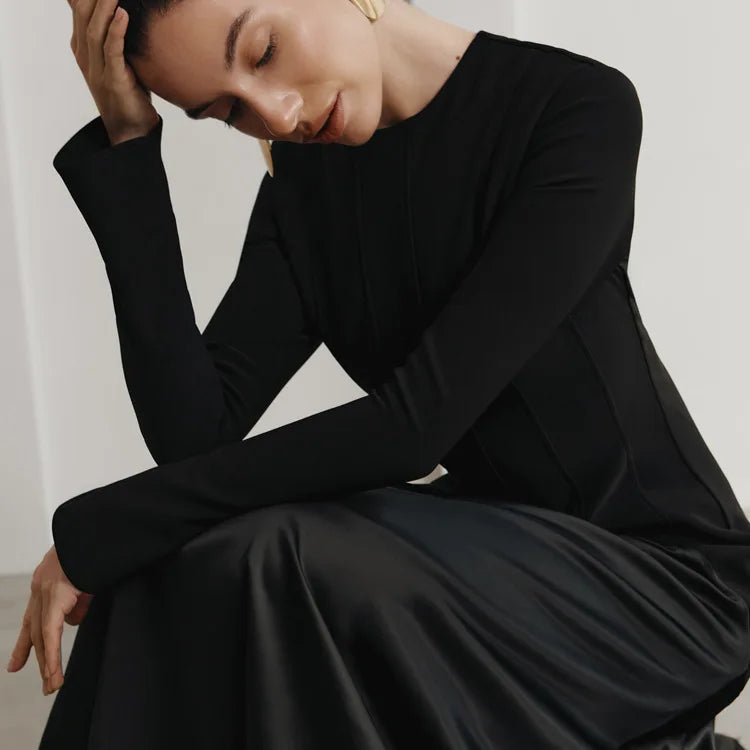 Woman wearing a black dress sitting against a plain background