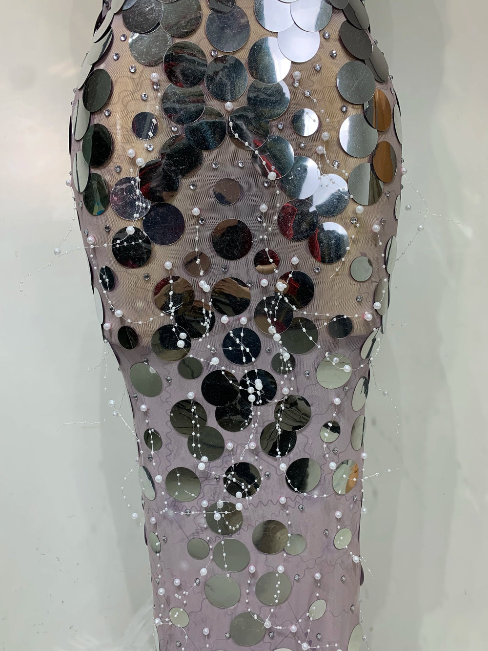 Mannequin wearing a dress covered in reflective sequins on a plain background
