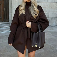 Woman wearing a brown coat and holding a black handbag on a city street.