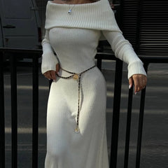 Person wearing a white ribbed sweater and skirt set with a belt, standing against a dark background.