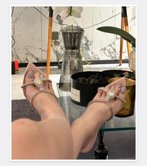 Close-up of feet wearing silver sandals with rings, in front of a decorative indoor setting.
