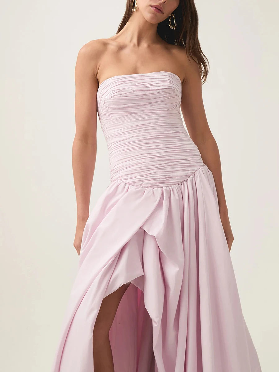 Woman wearing a strapless pink gown with a slit on a white background