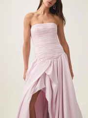 Woman wearing a strapless pink gown with a slit on a white background