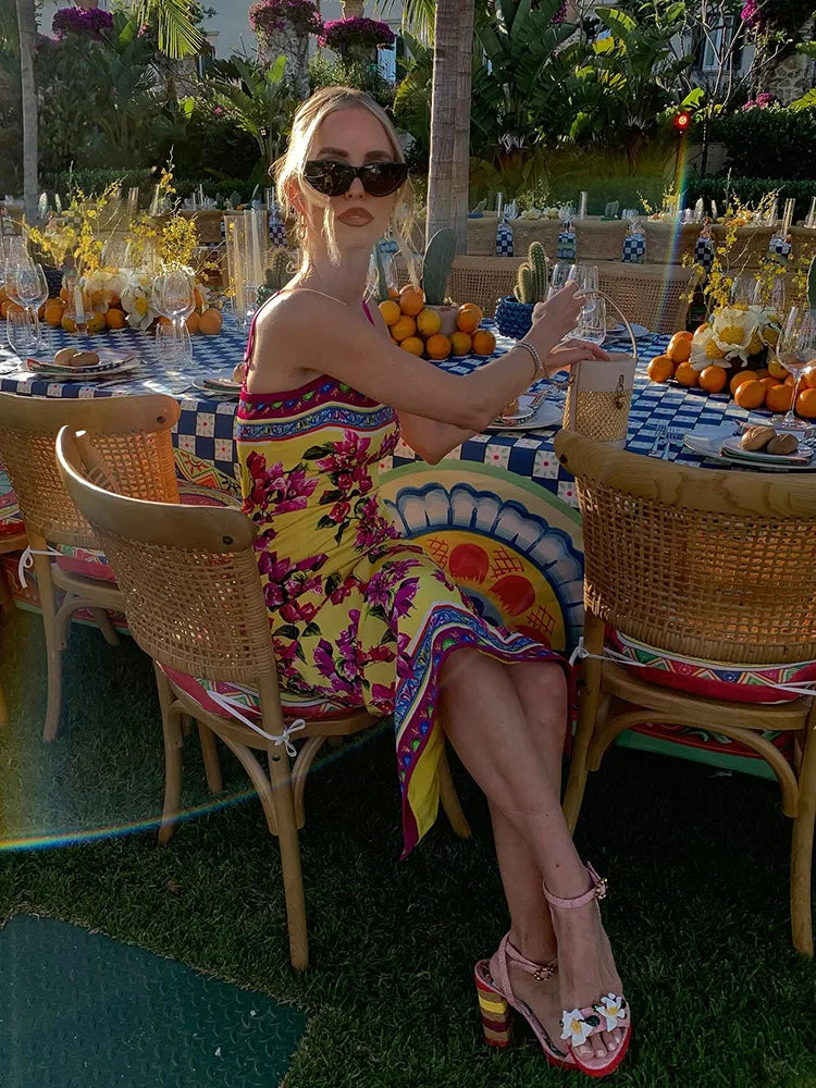Woman in a colorful dress sitting at an outdoor dining table with a tropical setting.