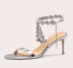 Silver high-heeled sandal with decorative chain on a white background