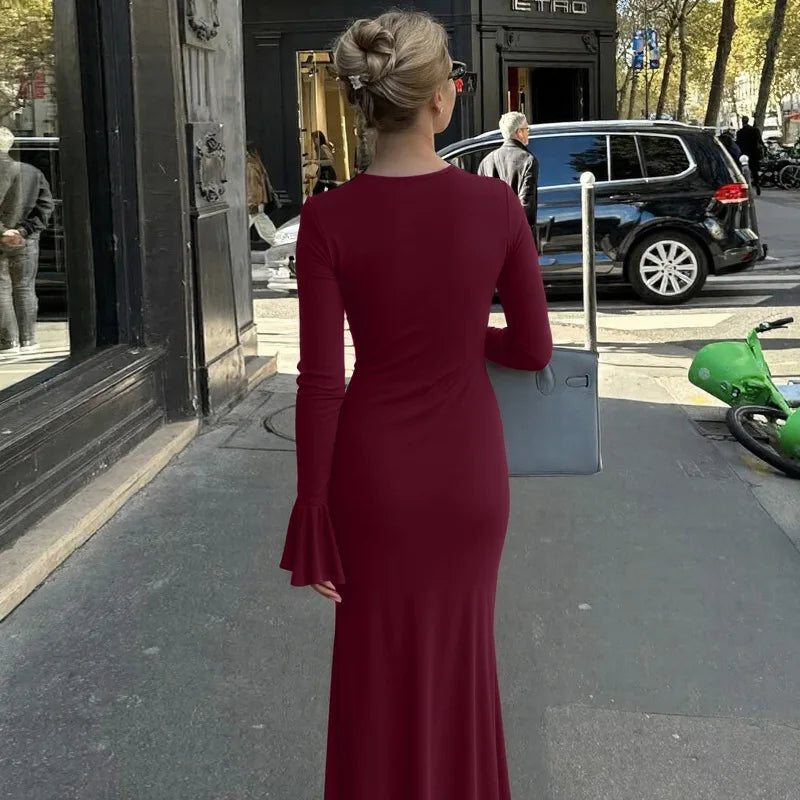 Woman in a red dress standing on a city street with a store and pedestrian in the background.