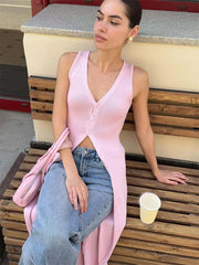 Woman sitting on a wooden bench wearing a pink sleeveless top and blue jeans, with a pink handbag and a white cup beside her.