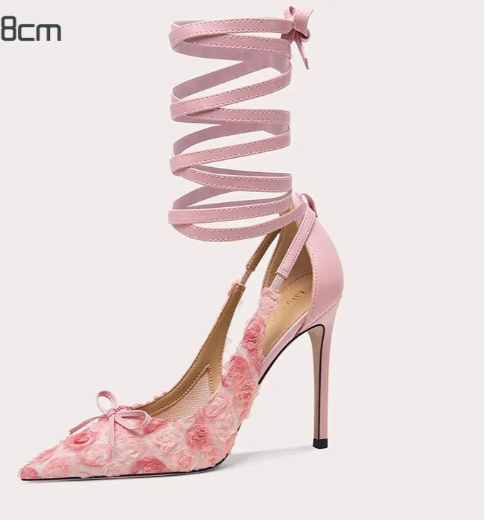 Pink high-heeled shoe with floral design and matching strap on a white background