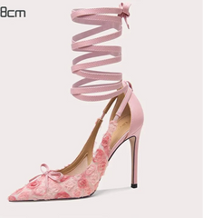 Pink high-heeled shoe with floral design and matching strap on a white background