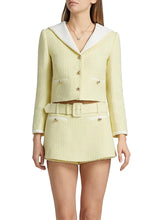 Woman wearing a light yellow tweed suit with a white shirt