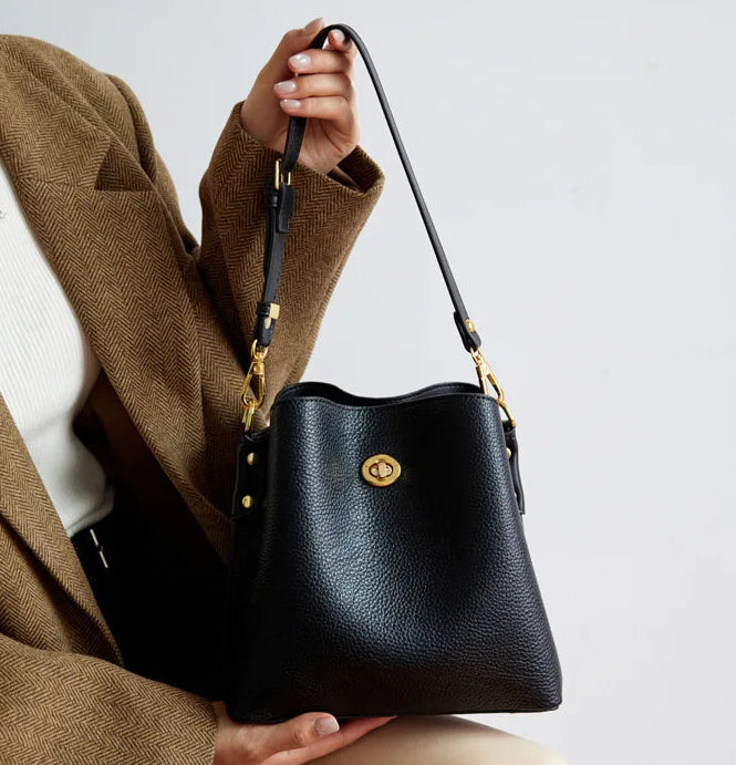 Person holding a black handbag with a gold clasp on a light gray background