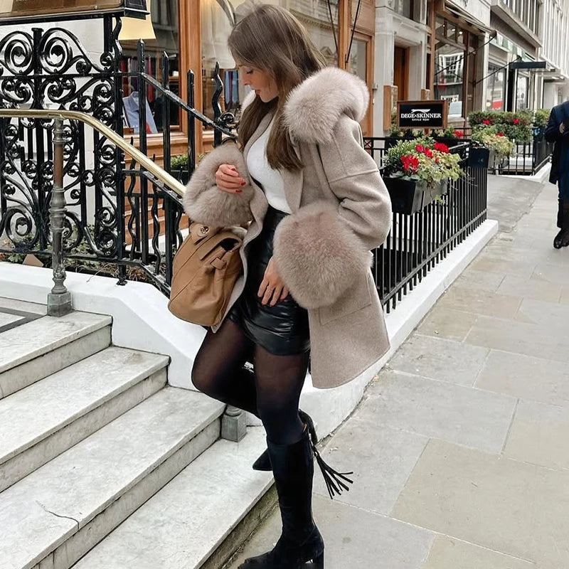 Woman in a fur-trimmed coat standing on a city street.