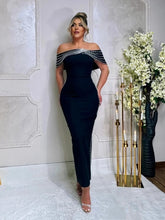 Woman wearing a black off-shoulder dress with white floral details in an elegant room.