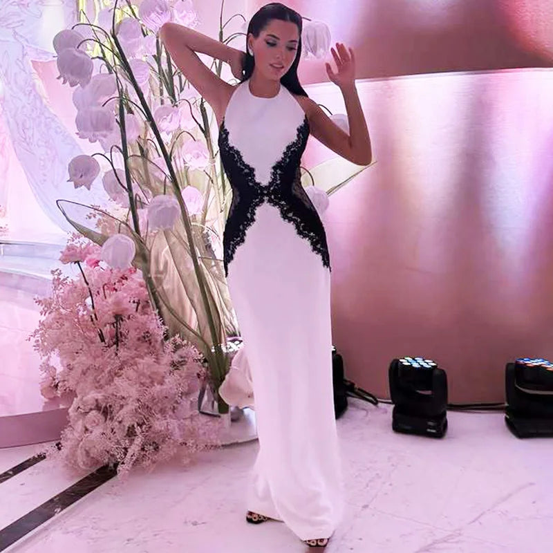 Woman in a white and black evening gown standing next to floral decorations.