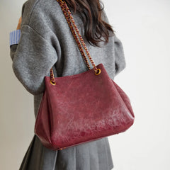 Person holding a red handbag with a chain strap against a neutral background