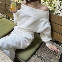 Person wearing a white off-shoulder outfit sitting on a wooden bench outdoors.