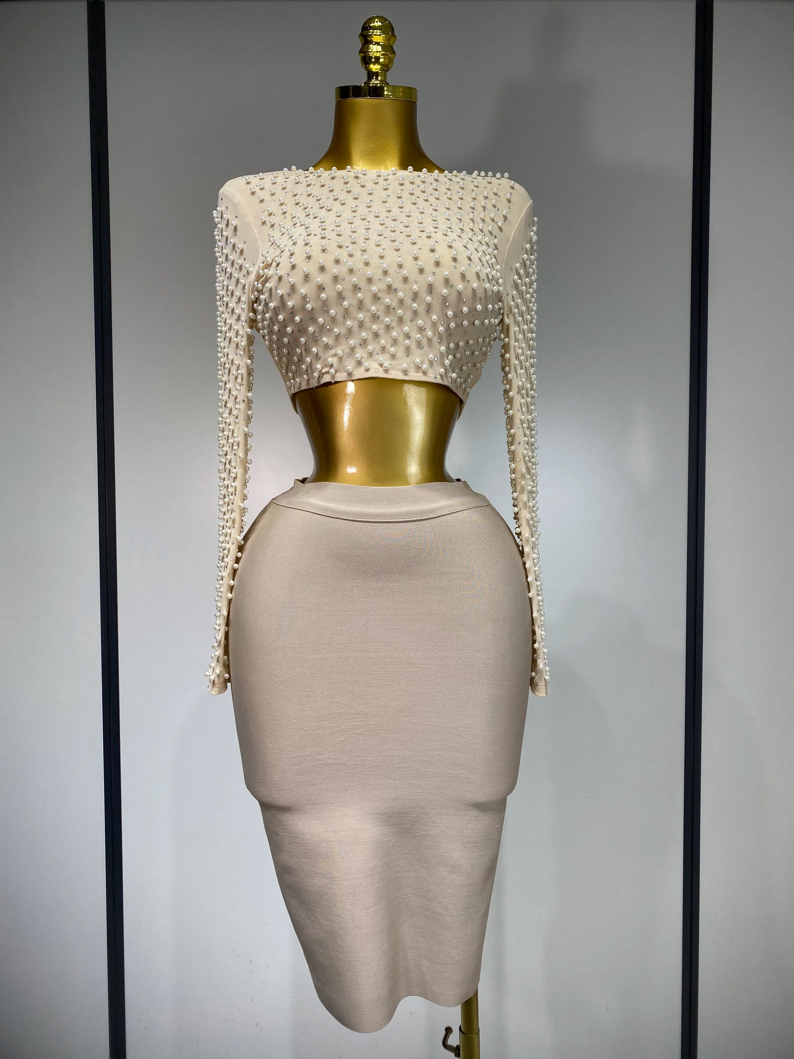 Mannequin wearing a beige dress with pearl embellishments on a plain background