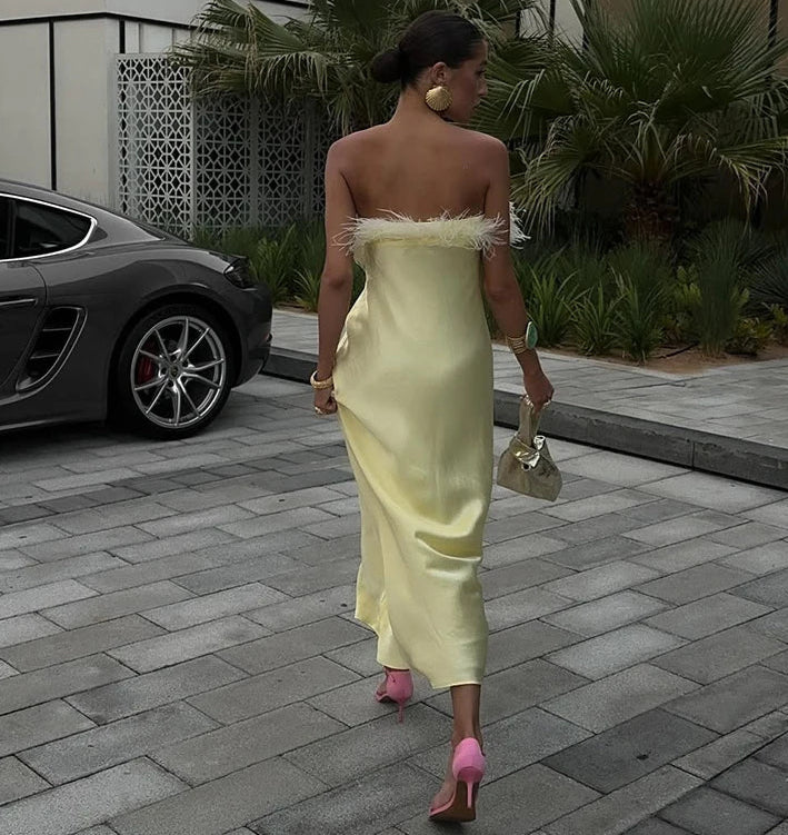 Woman in a light yellow dress with feathered shoulders walking on a paved area.