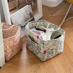 Floral fabric storage baskets on a wooden floor with items inside.