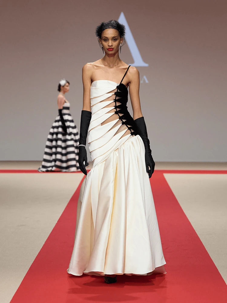 Model wearing a white evening gown with black accents on a red carpet