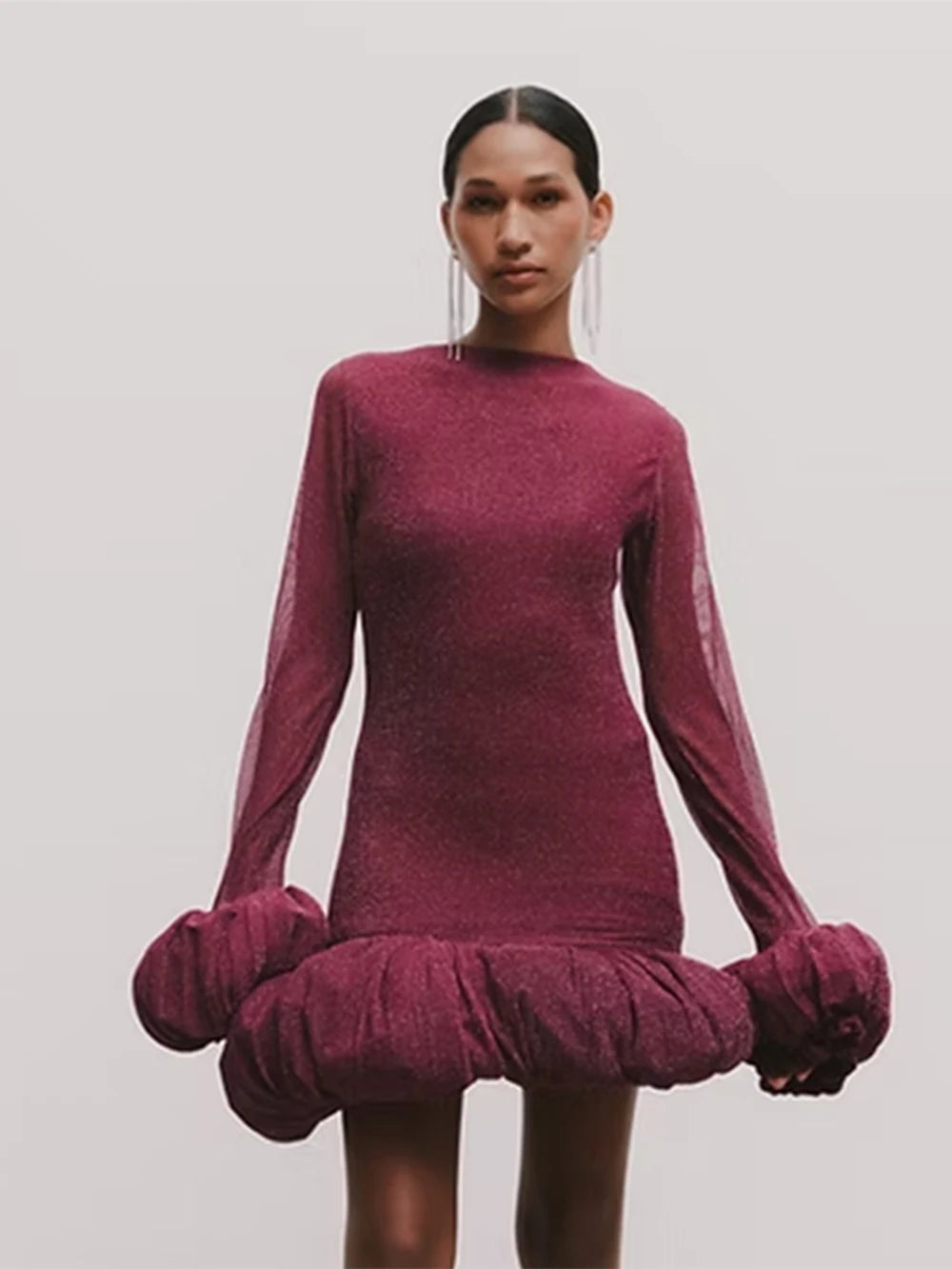 Model wearing a burgundy dress with long sleeves and a ruffled skirt on a plain background