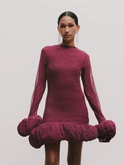 Model wearing a burgundy dress with long sleeves and a ruffled skirt on a plain background