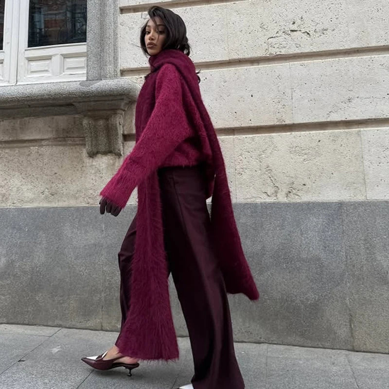 Woman wearing a long burgundy coat and pants standing against a stone wall.